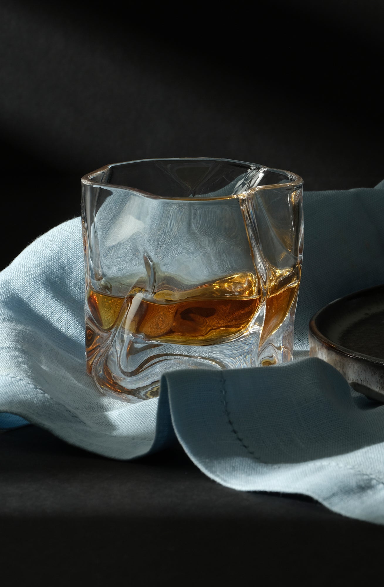 A Malt & Brew Whisky Wave Glass with a shot of whisky sits on a blue cloth.