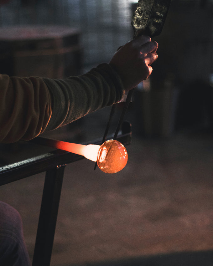 A glassblower squeezes red-hot glass into shape.