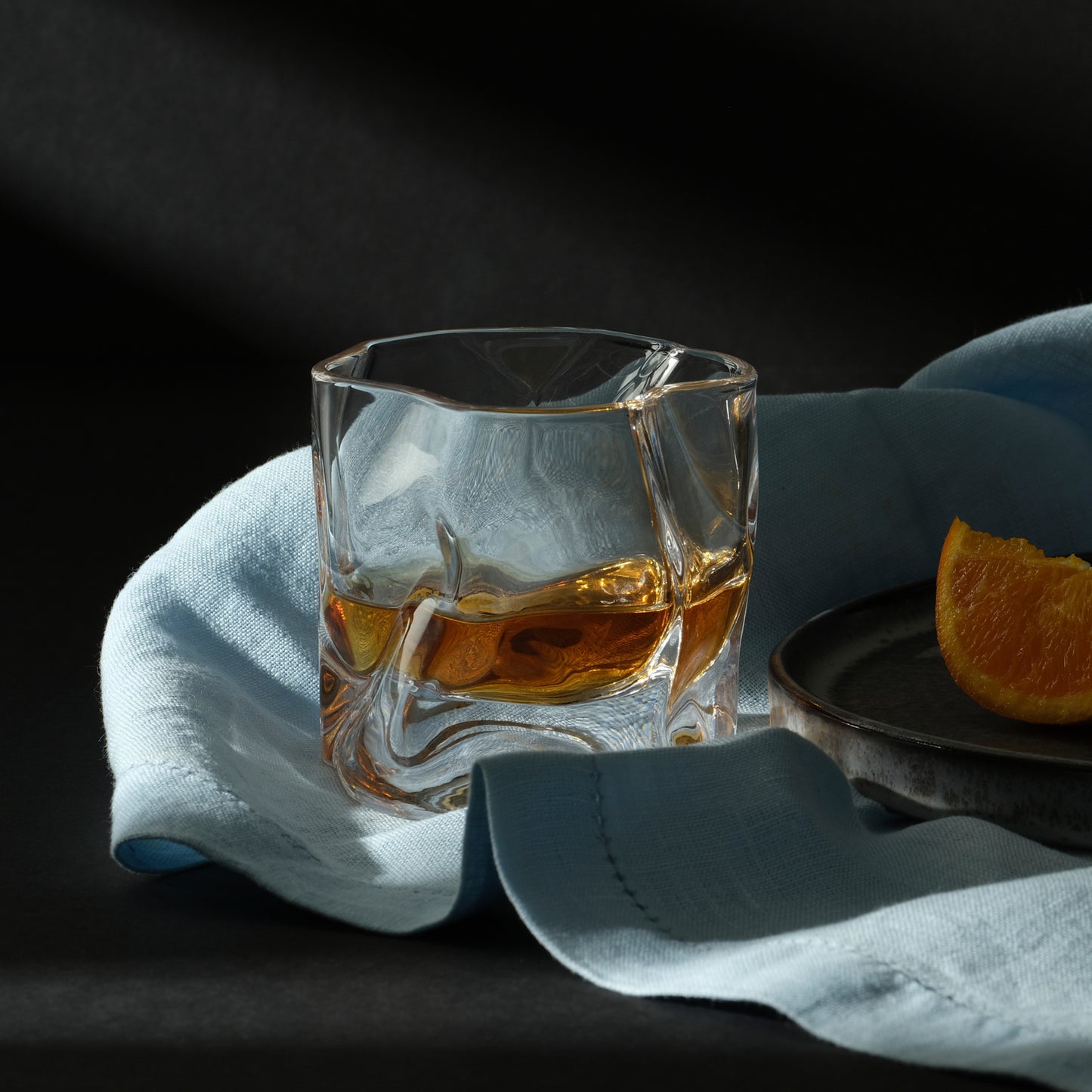 A Malt & Brew Whisky Wave Glass with a shot of whisky inside sits on a blue cloth.